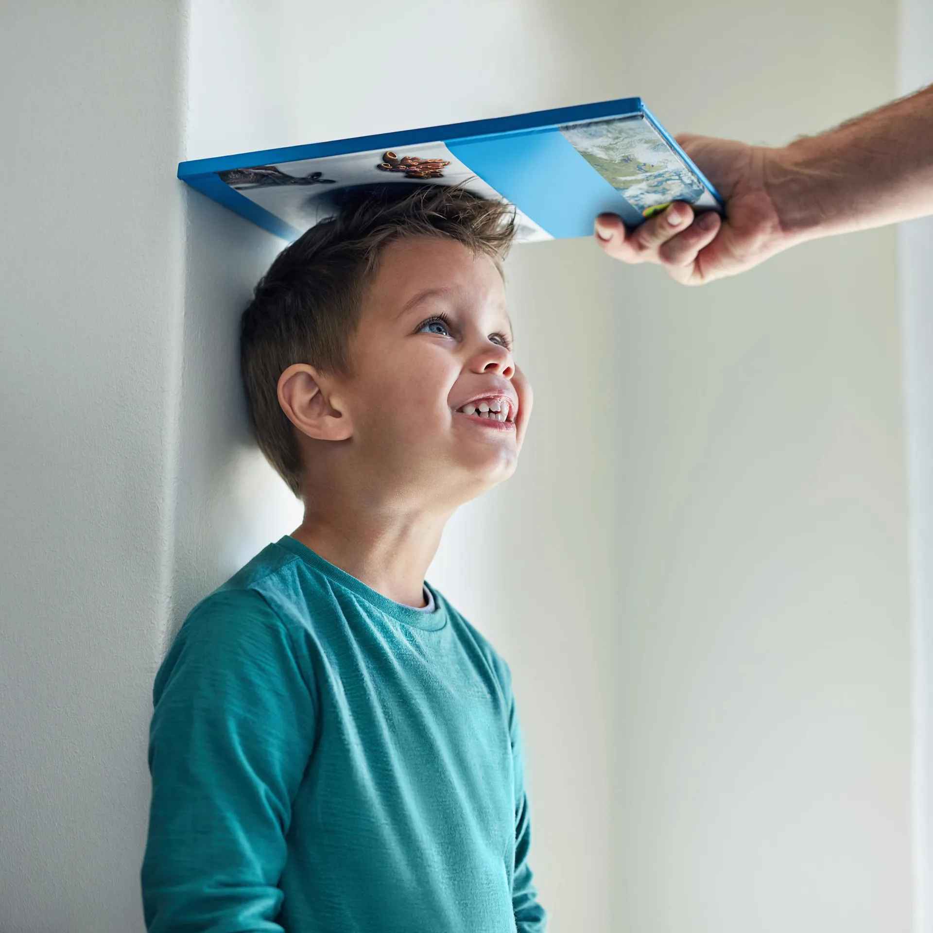 Menino sorrindo com livro apoiado na cabeça medindo altura