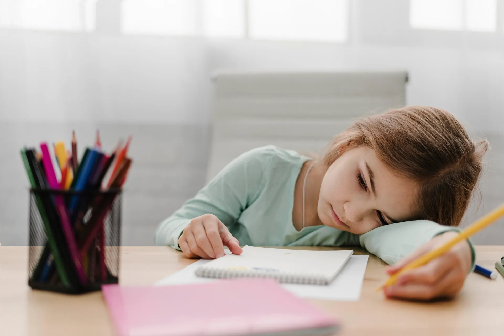 Menina cansada apoiada na mesa com material escolar