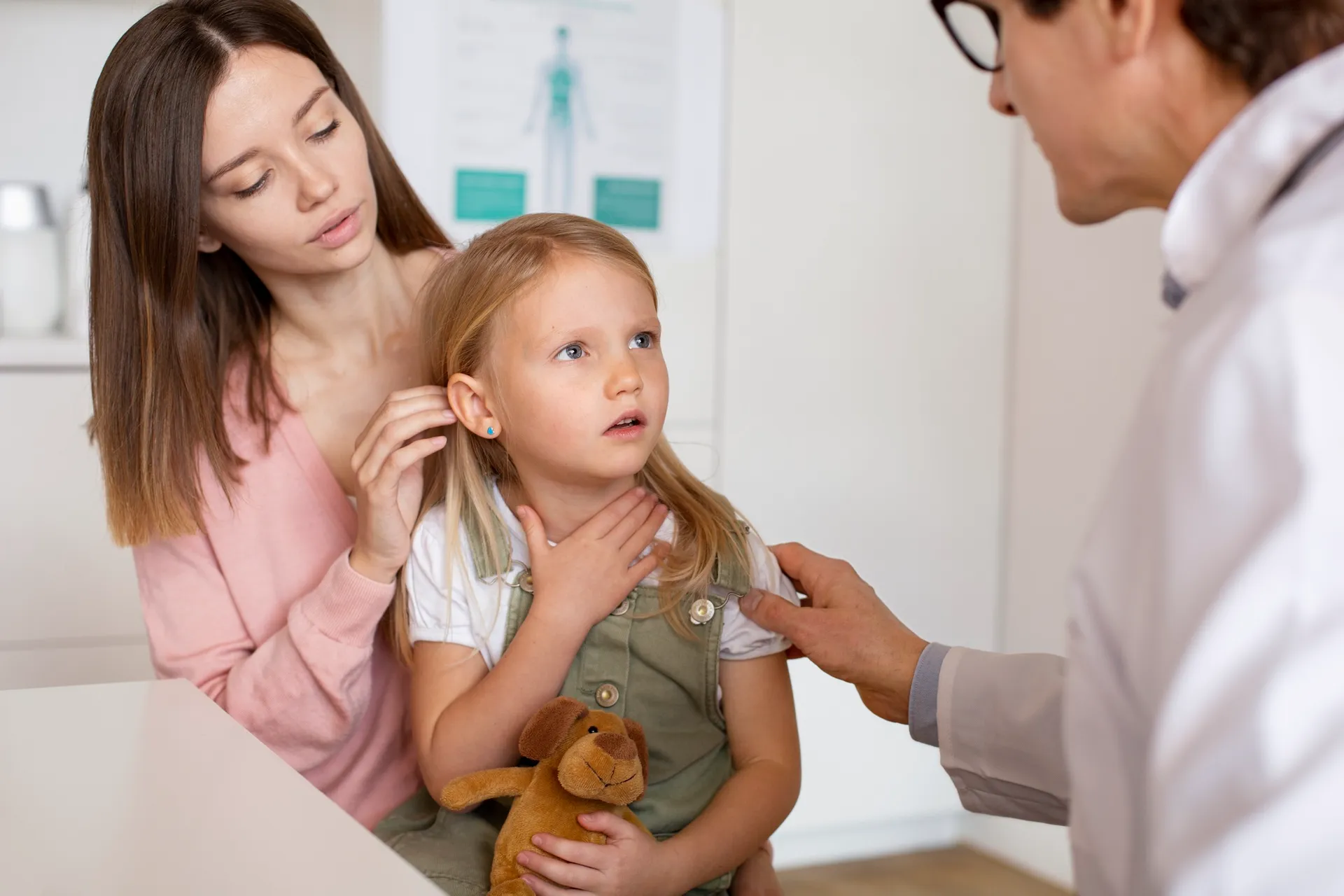Médica examinando pescoço de criança com a mãe ao lado